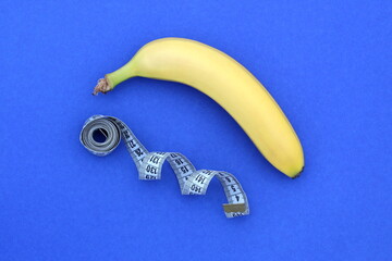 A yellow ripe banana with a centimeter flexible tape lies on a blue background.