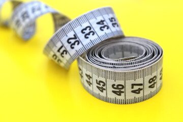 A twisted centimeter tape lies on a yellow background