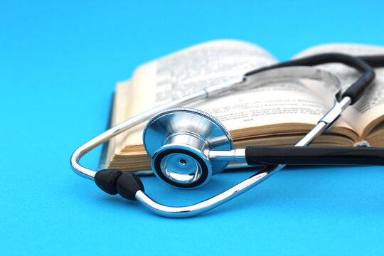 On a blue background lies a textbook with a stethoscope. Medical education theme. - Powered by Adobe