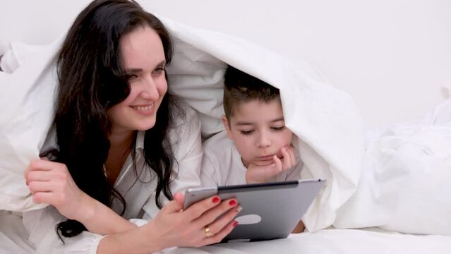 banner family Cosiness mom and son under white duvet playing on tablet concept heat heating electricity gas apartment payment buying a new house construction online study single mom social assistance