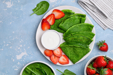 Green spinach crepes or pancakes with strawberries and sour cream on a plate. Healthy  food. Spring greenery dessert.  Top view, copy space