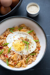 Bowl of korean kimchi fried rice topped with chicken egg, vertical shot on a black marble background, middle closeup