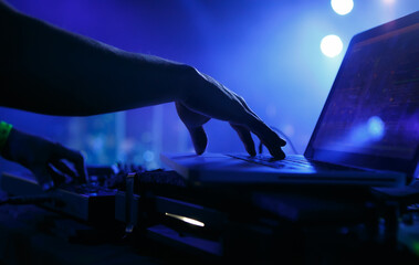 Club DJ playing music with laptop and midi controller. Hand of professional disc jockey mixing musical tracks on party in night club - obrazy, fototapety, plakaty