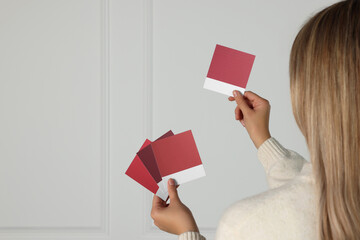 Woman choosing paint shade for wall indoors, focus on hands with color sample cards. Interior design