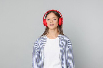 Teenage girl listening to music with red headphones on light grey background