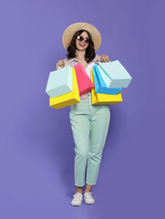 Beautiful young woman with paper shopping bags on purple background