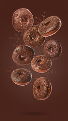 Many sweet tasty donuts with chocolate crumbs falling on brown background