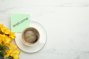 Welcome card, beautiful yellow freesia flowers and cup of aromatic coffee on white marble table,...