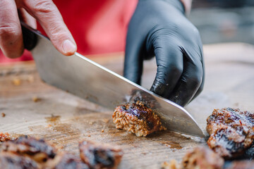 Close up of meat on Cutting board. Chef cuts juicy low-roasted meat with large kitchen knife. Blurred background. Soft focus