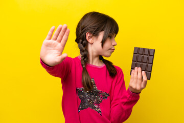 Little caucasian girl with chocolat isolated on yellow background making stop gesture and...