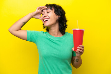 Young Argentinian woman holding a soda isolated on yellow background smiling a lot