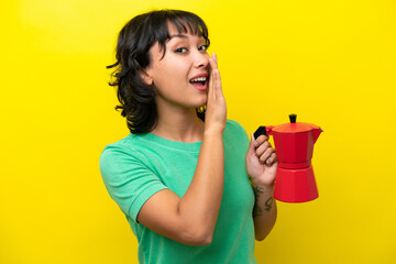 Young Argentinian woman holding coffee pot isolated on yellow background whispering something