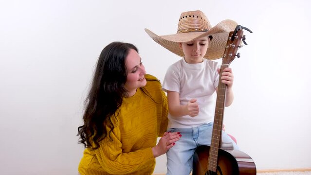 mom and son on a white background in studio boy plays guitar In a huge Mexican hat little cowboy mom smiles admiring touches child tenderness care entertainment children musical instruments image