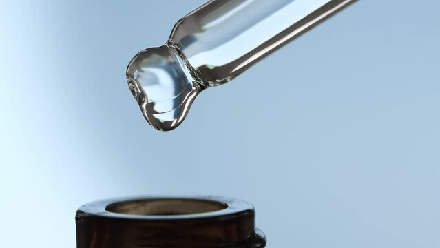 A drop of essential oil for massage and spa slowly dripping into a brown cosmetic bottle, macro, front view.