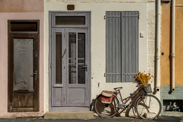 Fototapeta na wymiar Vintage bicycle with spikelets in the basket parked in front of the old house facade in southern France. Relaxed street atmosphere of the sea village.