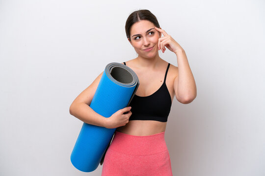 Young sport girl going to yoga classes while holding a mat isolated on white background having doubts and thinking