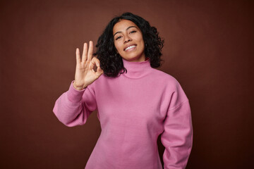 Young colombian curly hair woman isolated on brown background cheerful and confident showing ok...