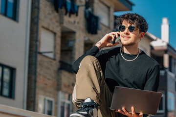 young man in the street outdoors with laptop and mobile phone