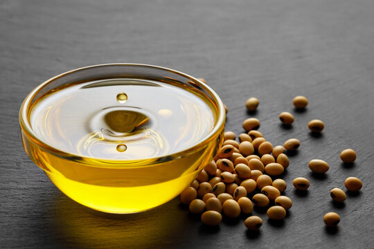 soybean oil with flying drop in bowl and beans on black stone background