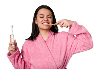 A woman in a pink bathrobe holds both an electric toothbrush and a traditional toothbrush, with a...