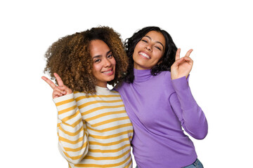 Two female friends isolated in studio joyful and carefree showing a peace symbol with fingers.