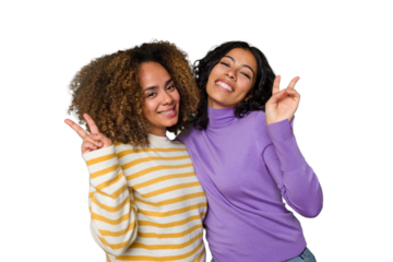 Two female friends isolated in studio joyful and carefree showing a peace symbol with fingers.