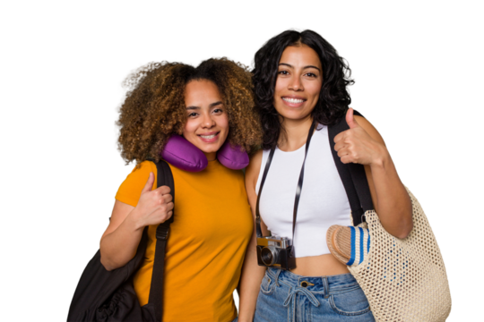 Two diverse friends on a beach vacation with vintage camera, beach bag, and travel pillow smiling and raising thumb up