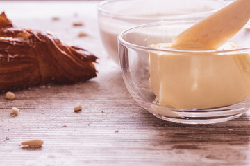 Butter in a glass bowl with a croissant on the left and milk in the background