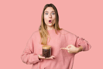 Young woman holding a container of coffee beans, symbolizing the energy and invigoration of this beloved beverage pointing to the side