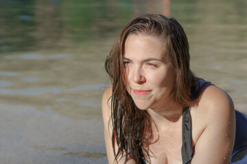 attractive young woman in a black swimsuit lying on the shore of a lake