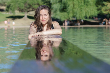attractive woman bathing in a lake, her face reflected in the water and smiles looking at the camera