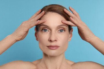 Naklejka premium Woman massaging her face on turquoise background