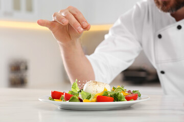 Obraz na płótnie Canvas Professional chef salting delicious salad at marble table, closeup