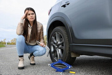 Fototapeta na wymiar Worried young woman near car with punctured wheel on roadside