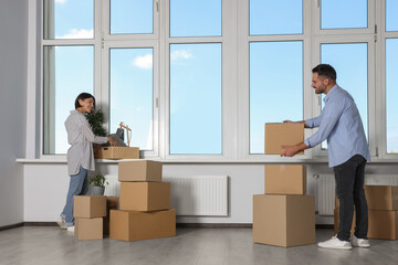 Happy couple with moving boxes near big window in new apartment