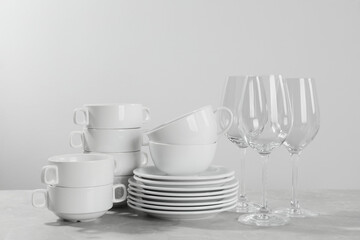 Fototapeta na wymiar Set of clean dishware and glasses on grey table against light background