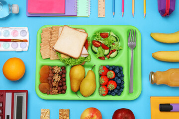 Flat lay composition with tray, tasty food and school stationery on light blue background