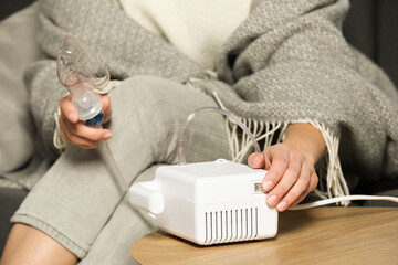 Woman using nebulizer at table indoors, closeup