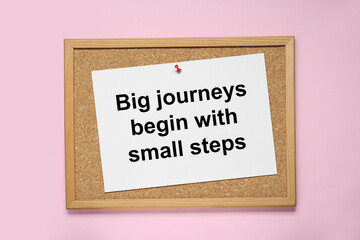 Corkboard with pinned message Big Journeys Begin With Small Steps on pink background, top view....