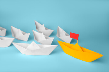 Group of paper boats following yellow one on light blue background. Leadership concept