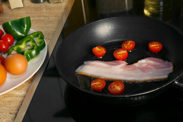 Cooking bacon with tomatoes in frying pan. Ingredients for breakfast