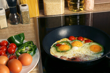 Cooking eggs with bacon, tomatoes and pepper in frying pan