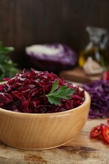 Tasty red cabbage sauerkraut with parsley on wooden table, closeup