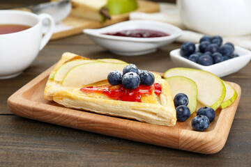 Fresh tasty puff pastry with jam, blueberries and pear on wooden table, closeup