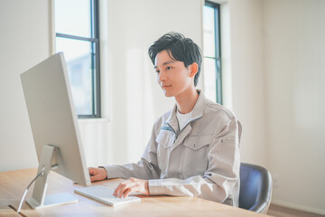 作業着を着てパソコン作業をする若いエンジニアの男性