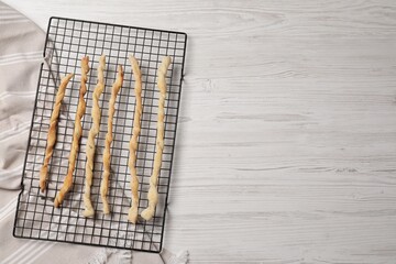 Rack with homemade breadsticks on white wooden table, top view and space for text. Cooking traditional grissini