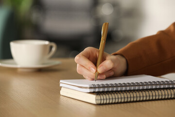 Woman writing in notebook at wooden table, closeup. Space for text