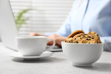 Chocolate chip cookies with cup of drink on table and office worker on background, closeup