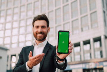Smartphone With Blank Screen In Businessman Hand, Smiling Middle Eastern Male Entrepreneur Showing For Mobile App Or Website Advertisement While Posing Outdoors, Mockup