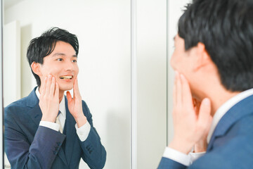 鏡の前で笑顔の練習をする若いサラリーマンの男性